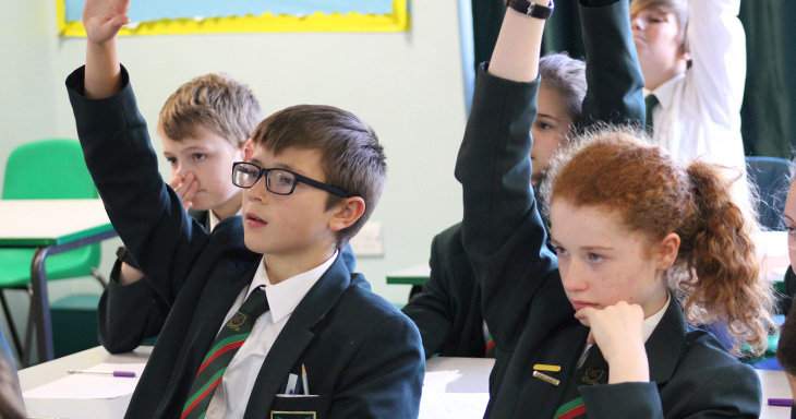 Pupils raise their hands in class.